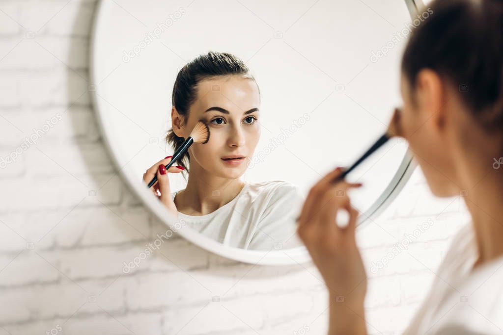 Beautiful female applying cosmetics on her face.