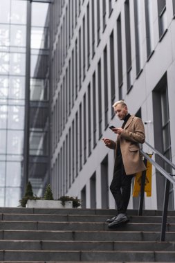 Genç Çekici İş Adamı Büyük Modern Ofis Binası 'nın yanında duruyor. Akıllı telefonuna bir İleti Yazıyor.