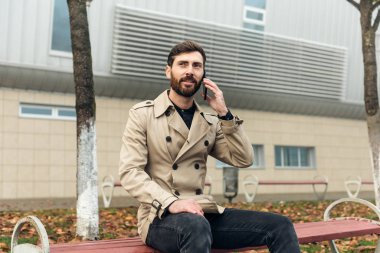 Gülümseyen yetişkin bir adam cep telefonu kullanıyor. İş adamı telefonda konuşuyor.