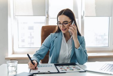 İş kadını yapışkan notlar yazarken cep telefonuyla konuşuyor.