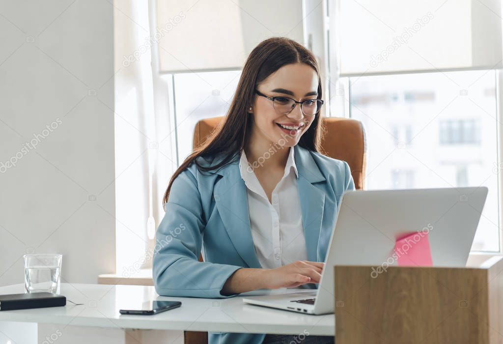 Portrait of beautiful cheerful young businesswoman working on laptop