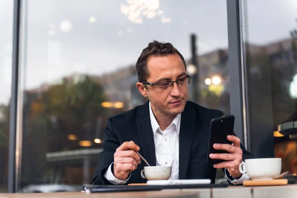 Empresario en la cafetería al aire libre bebiendo taza de café mientras usa el teléfono móvil — Foto de Stock