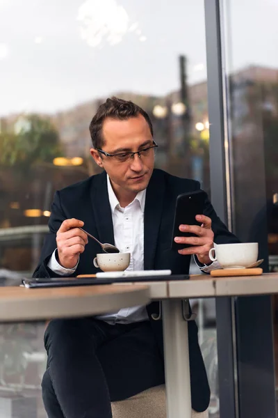 Empresario en la cafetería al aire libre bebiendo taza de café mientras usa el teléfono móvil — Foto de Stock