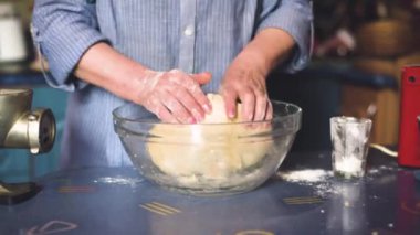 Ev mutfağında hamur işi pişiren kıdemli bir kadın. Büyükanne yemek pişiriyor, un hamuru hazırlıyor, büyükanne elleri kapalı. Üst düzey bir kadın kendi mutfağında hamur işi pişiriyor..