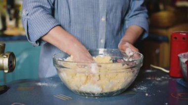 Büyükanne yemek pişiriyor, un hamuru hazırlıyor, büyükanne elleri kapalı. Ev mutfağında hamur işi pişiren kıdemli bir kadın. Büyükanne yemek pişirir, hamuru un içinde hazırlar, büyükanne elleri kapalı..