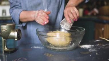 Ev mutfağında hamur işi pişiren kıdemli bir kadın. Büyükanne yemek pişiriyor, un hamuru hazırlıyor, büyükanne elleri kapalı. Üst düzey bir kadın kendi mutfağında hamur işi pişiriyor..