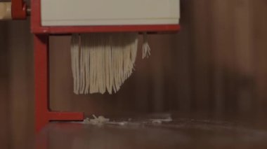 Ev yapımı erişte yapmak için el yapımı erişte makinesi kullanan yaşlı bir kadının fotoğrafı. Makarna makinesinden taze makarna geliyor. Yavaş çekim.