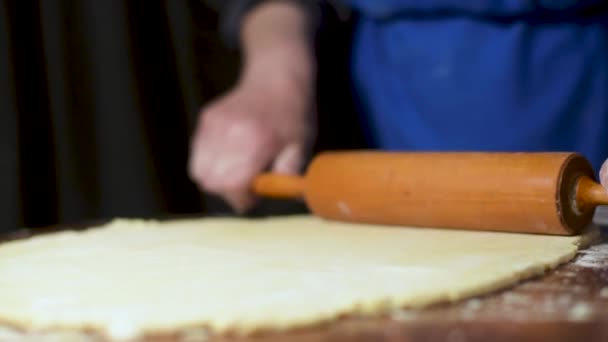 Rol het rauwe deeg uit op een houten plank bedekt met bloem met een deegroller van dichtbij — Stockvideo