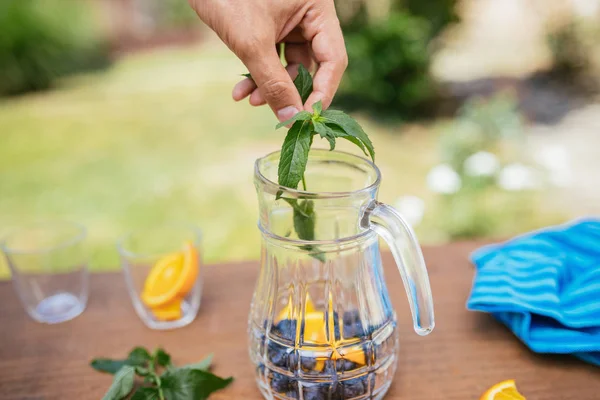 Colocando hortelã na garrafa de vidro com mirtilos e laranja — Fotografia de Stock