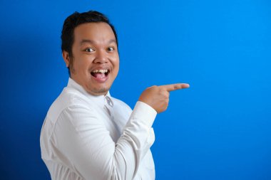 Asyalı mutlu ofis çalışanının portresi gülümsüyor ve mavi arkaplan fotokopi alanı olan bir şeyi kendi tarafında sunuyor.