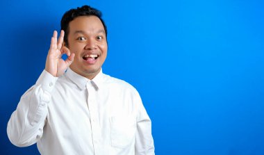 Genç Asyalı işadamı tamam işareti gösteriyor. Mavi duvara karşı vücut portresini kapat