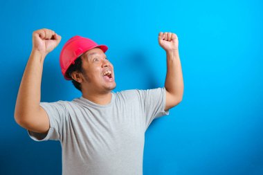 Ellerini sıkarken kameraya bakan kasklı şişko Asyalı adam. Adam zafer jesti yaptı.