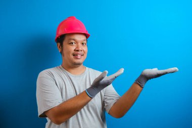 Miğfer takan şişman Asyalı adam yan yan bakarken elinde bir şey gösteriyor. Adam sevinç ve şaşkınlık ifadesi gösterdi.