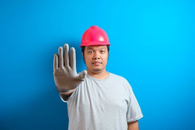 Asyalı şişman işçi el hareketini durdurdu. Tulumlu ve koruyucu miğferli işçiler eldivenli el hareketlerini durduruyor.