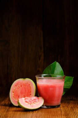 kırmızı guava suyu guava meyve dilimleri ve yaprak süslemeleri ile ahşap bir arka planda servis edilir.