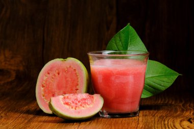 kırmızı guava suyu guava meyve dilimleri ve yaprak süslemeleri ile ahşap bir arka planda servis edilir.