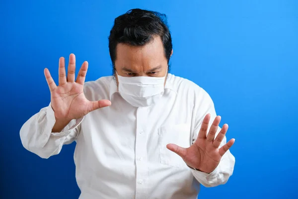 a fat Asian man wearing a mask to prevent transmission of the corona virus, by hand symbolizing stop gesture