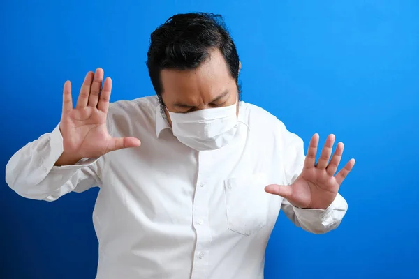 a fat Asian man wearing a mask to prevent transmission of the corona virus, by hand symbolizing stop gesture