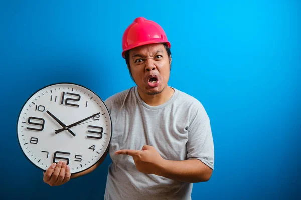 Fat Asian man uses an angry expression while pointing his finger toward the clock because the worker is late coming to the job site. Overworked concept