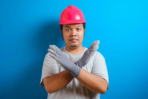 Asian fat worker shows stop hand gesture. Worker in overalls and protective helmet shows stop gesture with gloved hand