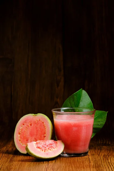 red guava juice is served on a wooden background with guava fruit slices and leaf decorations