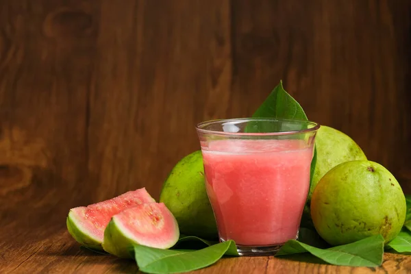 red guava juice is served on a wooden background with guava fruit slices and leaf decorations