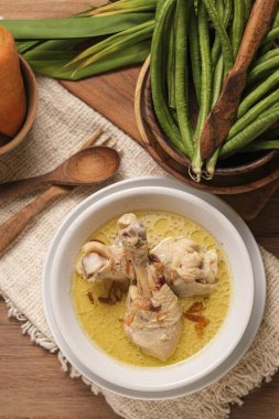 Opor Ayam ahşap bir masada servis edilir. Opor, hindistan cevizi sütü sosuyla pişirilmiş geleneksel Endonezya yemeğidir.