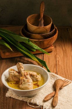 Opor Ayam ahşap bir masada servis edilir. Opor, hindistan cevizi sütü sosuyla pişirilmiş geleneksel Endonezya yemeğidir.