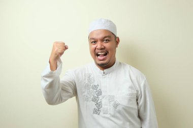 Asyalı Müslüman adam zafer jesti ile kameraya bakarak gülümsedi. Fildişi arkaplanda izole edilmiş