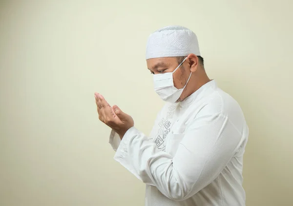 Asian Muslim man wearing mask praying with an empty space next to him. the man showed a solemn prayer movement