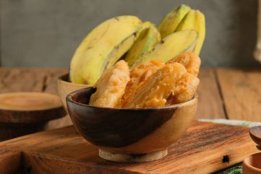 Pisang Goreng ahşap masada servis yaptı. Güney Doğu Asya 'da özellikle Malezya ve Endonezya' da popüler sokak yemekleri. Tatlı hamurla kaplanmış kızarmış muzdan yapılmış.