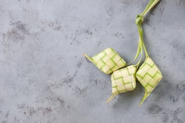 Ketupat 'ın üst görüntüsü tamamlanmamış gri duvar arkaplanından izole edildi. Oyuncak hindistan cevizi yapraklarından yapılmış pakete sarılmış pilavdan yapılan tipik bir yemek..