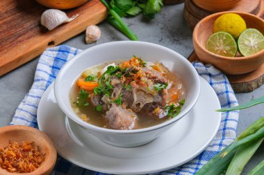 Sop buntut or oxtail soup is served in white bowl on rustic grey background. indonesian traditional culinary clipart