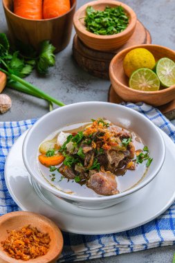 Sop buntut ya da öküz kuyruğu çorbası beyaz kasede kırsal arka planda servis edilir. Endonezya Geleneksel Aşçılık