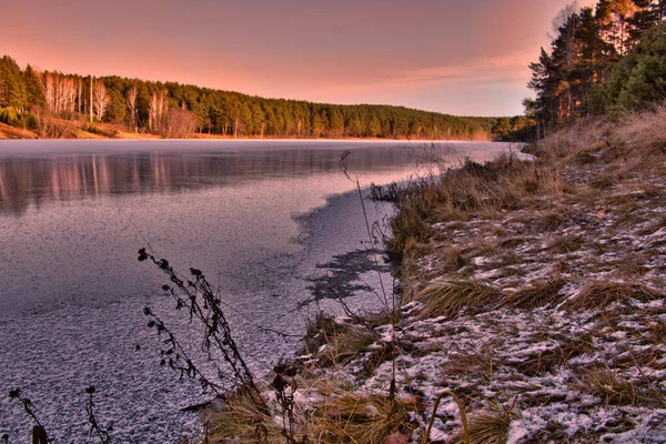 Puesta de sol en el bosque de invierno. bosque a orillas del río congelado. hielo en el río — Foto de Stock