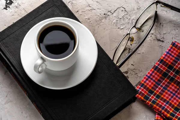 Lire un livre intéressant autour d'une tasse de café. tasse de café, livre et verres avec une serviette sur un fond de béton gris. pause café au travail ou à l'école — Photo