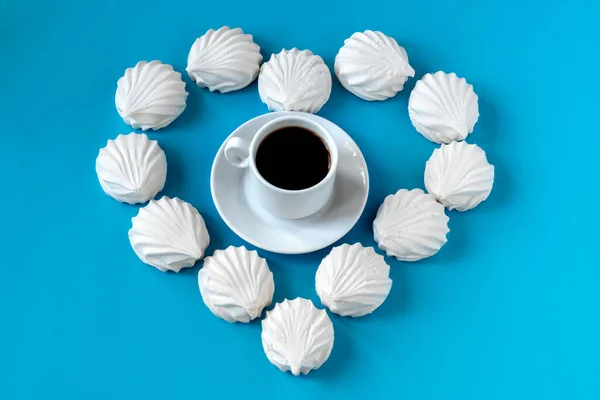 Guimauves à la vanille blanche disposées sur un fond bleu sous la forme de cœurs et au centre est une tasse de café aromatique noir. petit déjeuner pour un être cher . — Photo