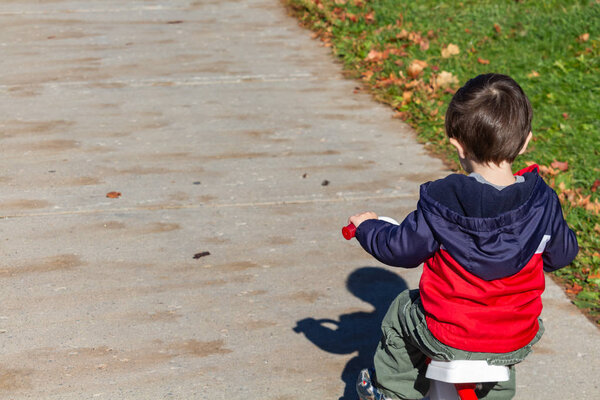 Little Boy Rides His Tricycle Away on a Sidewalk