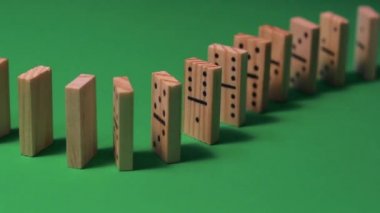 Tahta domino taşları domino gösterisi için dizilir ve çabucak yıkılır. Yeşil arka planda, belirgin gölgelerle duruyorlar..
