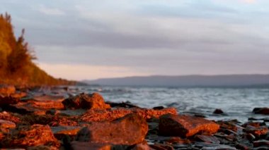 Sabahın ilk ışıklarıyla yıkanan dalgalar, nehrin kayalık kıyısındaki kayalara çarpıyor..