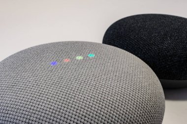 Google Nest Mini akıllı konuşmacısının yakın plan görüntüsü renkli ışıklarının etkinleştiğini ve arkasında başka bir Yuva Mini 'nin oturduğunu gösteriyor..