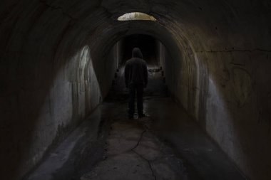 Bilinmeyen karanlığa giden bir adamın silüeti karanlık, eski, karanlık bir yeraltı geçidinde tavandaki bir kapaktan güneş ışığıyla aydınlatılıyor..