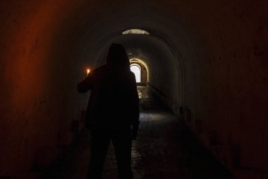 Kapüşonlu adam elinde mumla karanlık yeraltı geçidinden bir çıkış yolu buldu ve tünelin sonundaki ışıklı kapıya gitti..