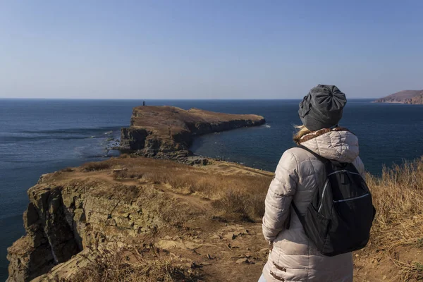 Sırt çantalı bir kadın turist güneşli bir bahar gününde Vladivostok 'taki Tobizin Burnu' nun pitoresk sahilinde denize bakıyor..