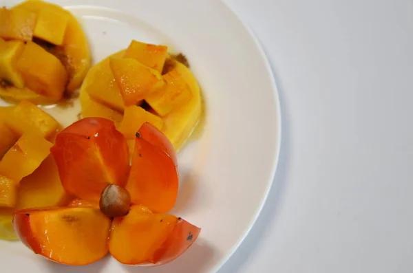 Vegetarian Diet Food. On a white plate are slices of baked pumpkin with honey and cinnamon and ripe sweet persimmons.