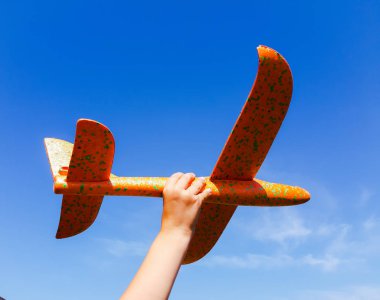 Mavi bulutsuz gökyüzü. Turuncu renkli oyuncak uçak bir çocuğun elinde..