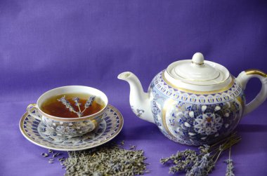 Lavanta Kraliçesi Aromaterapisi. Mor arka planda, bir çaydanlık, çay, filiz ve kurutulmuş lavanta..