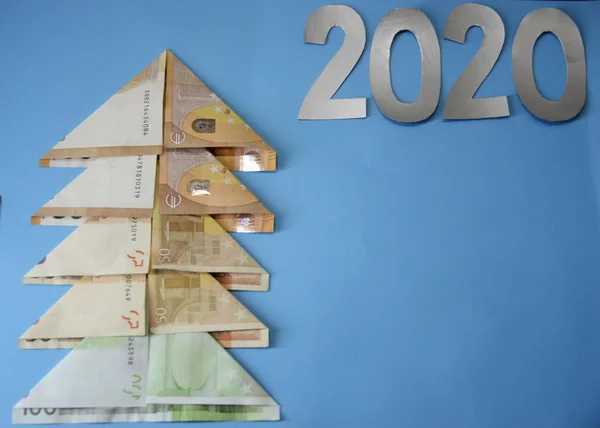 New Year. Holiday. Business and finance. Backgrounds and textures. On a blue background is a Christmas tree made of banknotes and numbers 2020.