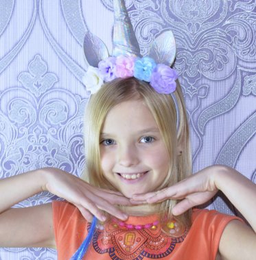 Mavi gözlü ve sarı saçlı güzel bir kızın portresi. Kafasında bir çiçek çelengi ve bir tek boynuzlu at var..