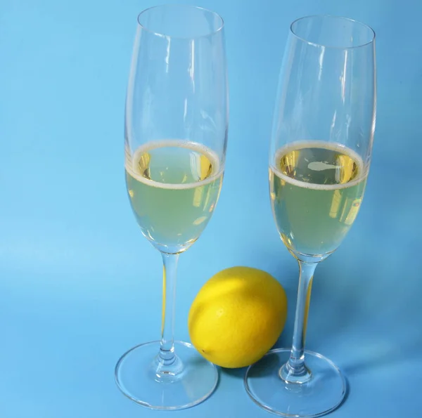 Glasses with champagne stand on a blue background, a yellow lemon lies.